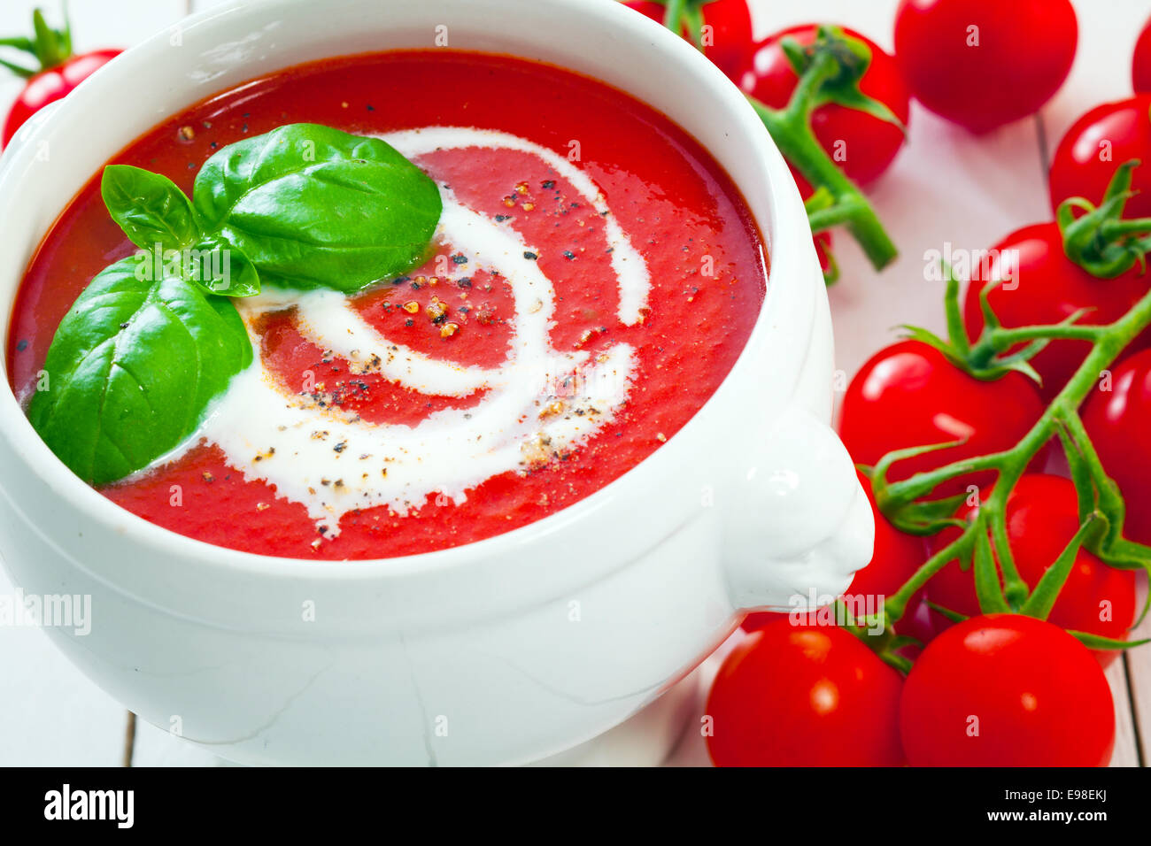 Pomodori freschi con una gustosa minestra di pomodoro spruzzata con panna e cosparsi di pepe macinato e rabboccato con basilico fresco Foto Stock