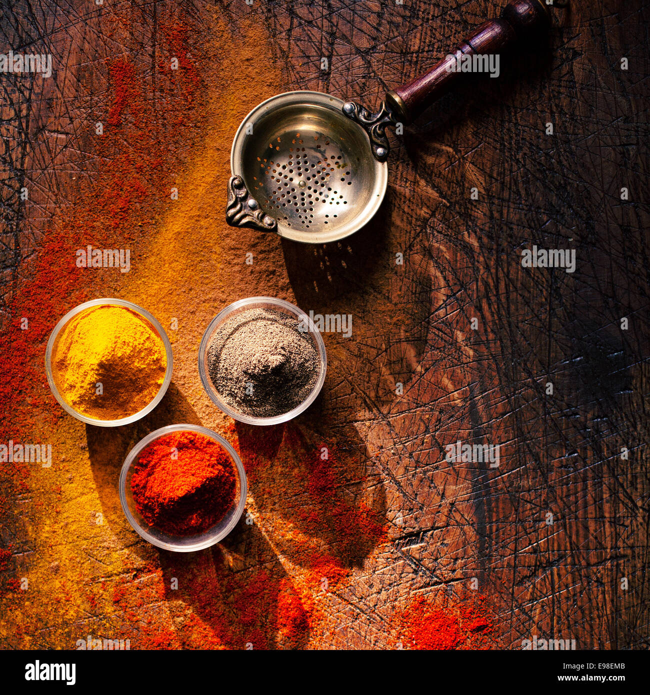 Vista aerea di tre bocce di spice in una cucina di paese su un vecchio ha segnato una superficie di legno con sparsi in polvere e una vecchia succhieruola retrò o setaccio Foto Stock