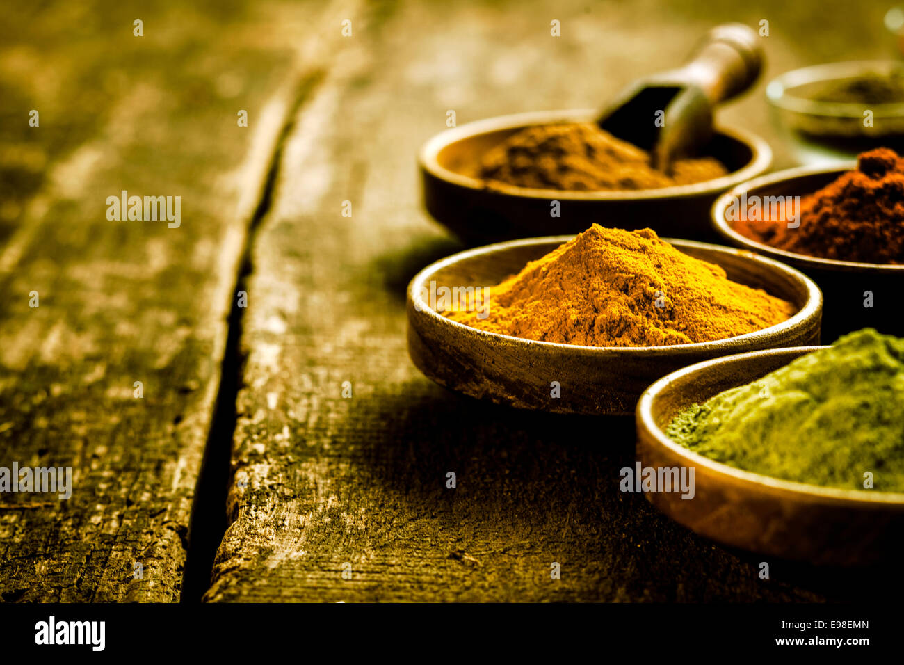 Messa a fuoco selettiva di una ciotola di asiatici di curry in polvere su vecchie tavole di legno fra una serie di altre spezie di terra, con copyspace Foto Stock