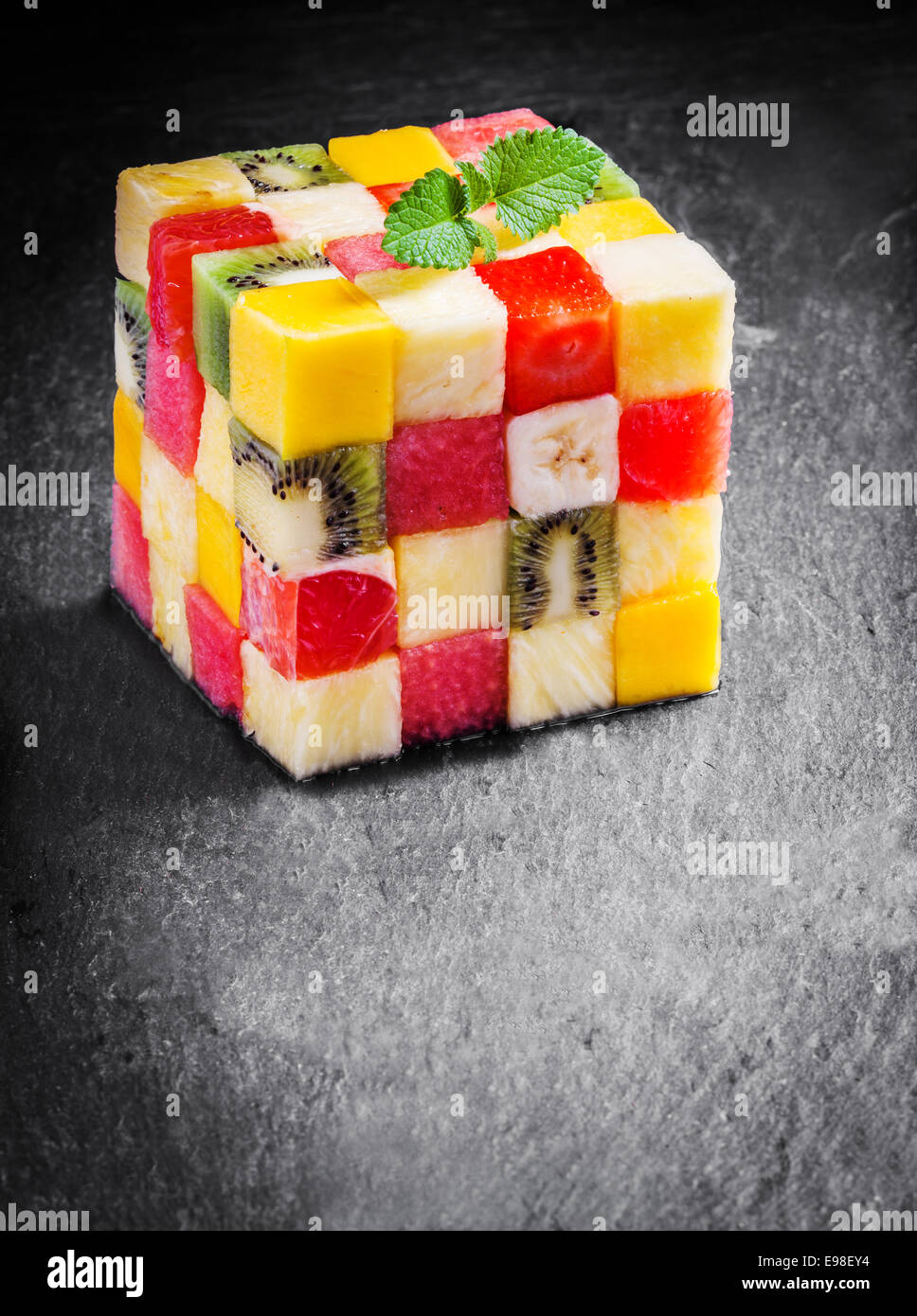 Colorato cubo gourmet di dadini di frutta fresca tropicale con cocomero melone, arancia, fragola, banana, kiwi e apple guarnito con menta su una cucina in ardesia con contatore copyspace Foto Stock