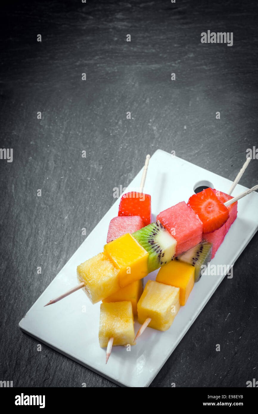 Trio di frutta fresca spiedini con cubetti di fragola, melone, anguria, kiwi e ananas su spiedini di legno servita su una piastra, ad alto angolo di visione su ardesia con copyspace Foto Stock