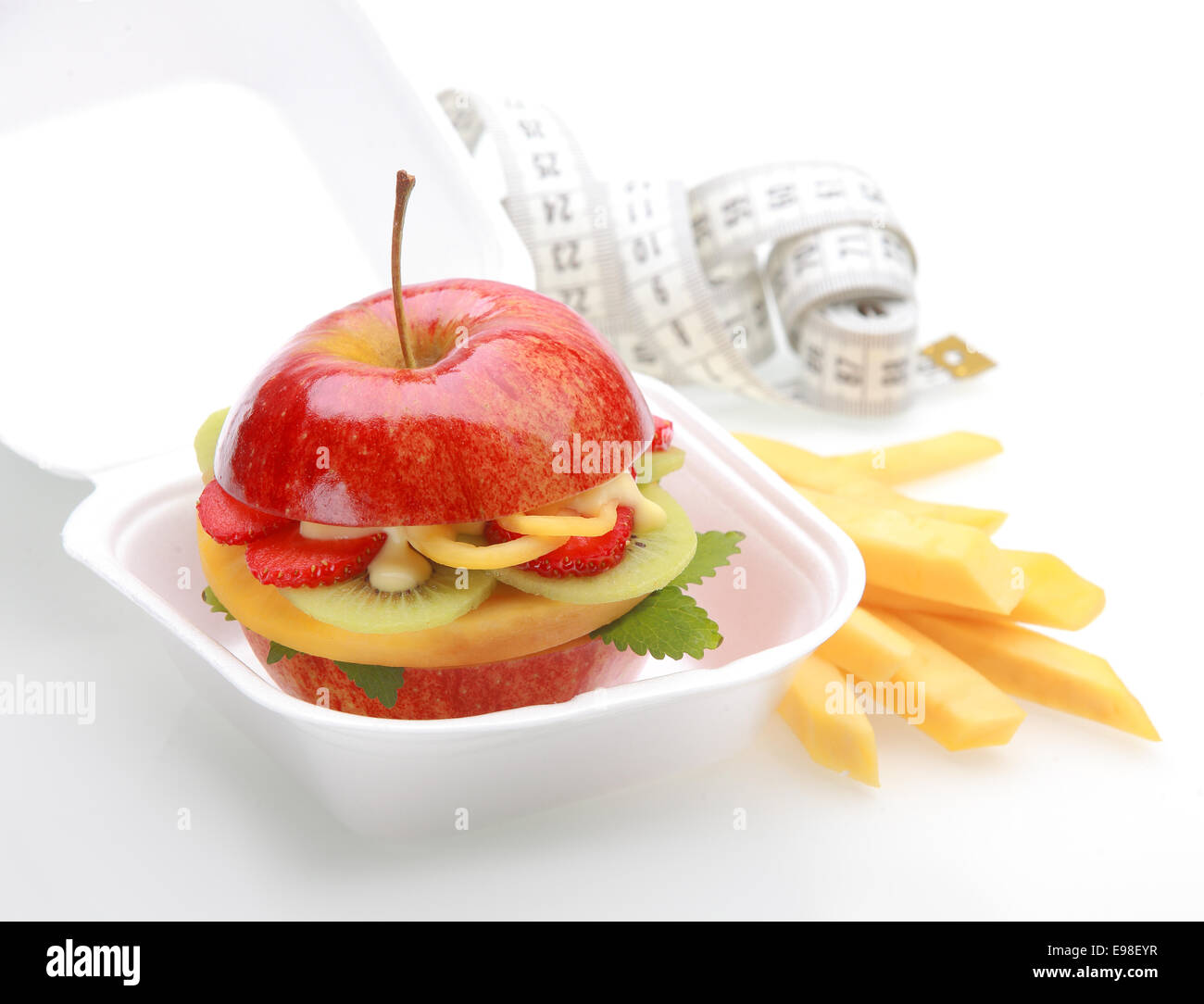 Un sano hamburger di apple da asporto in un fast food contenitore con una succosa mela rossa attraverso a fette e riempito con dadolata di frutta fresca tropicale e salsa di frutta con bastoni o trucioli e un metro a nastro Foto Stock