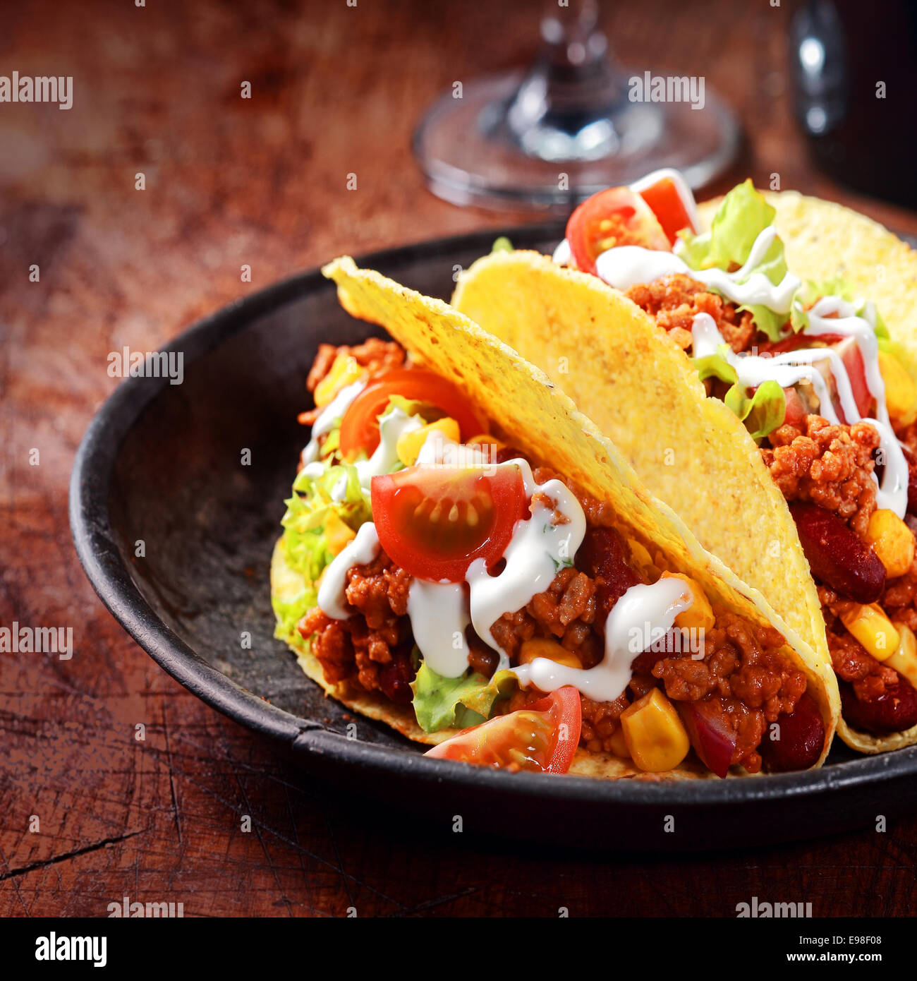 Golden Crisp tortilla di mais o taco ripiena di carne , insalata e verdura e spruzzata con panna acida o mayo servita in un ambiente rustico ciotola di legno, close up del riempimento Foto Stock