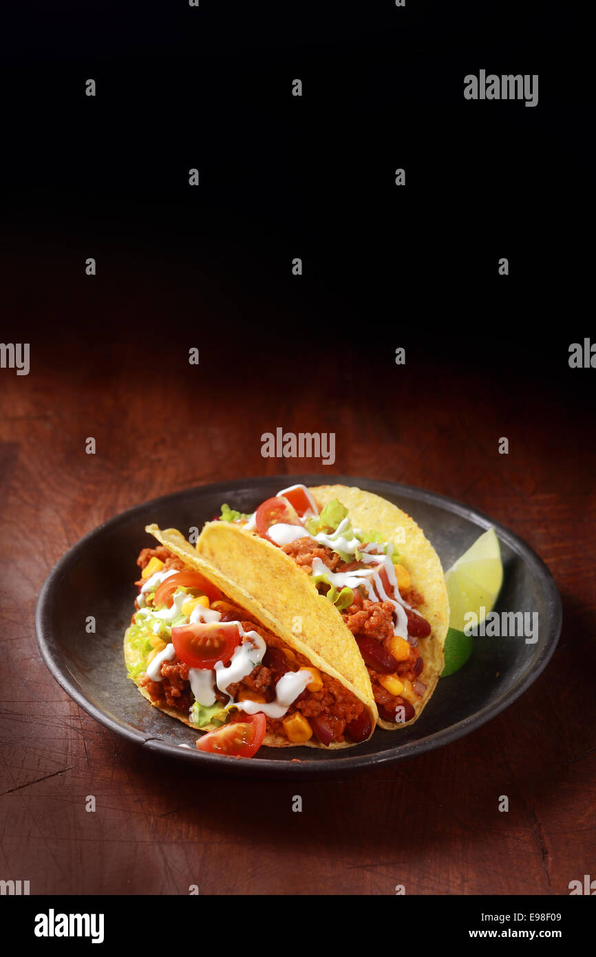 Mais messicano taco riempiti con carne macinata speziata , salsa e insalata servita in un poco profondo la ciotola di legno su una tavola di legno con copyspace Foto Stock