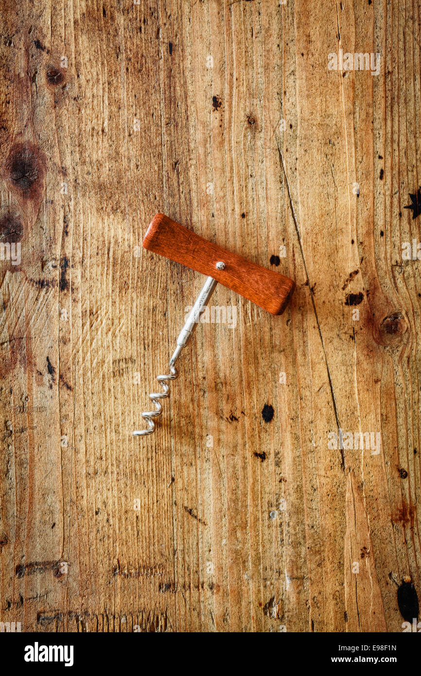 Cavatappi manuale con un manico in legno e vite in acciaio per aprire le bottiglie di vino giacenti centrato su una trama della superficie in legno con copyspace Foto Stock