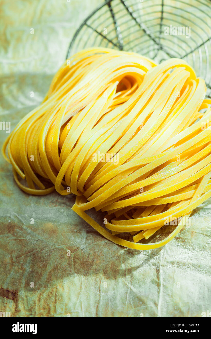 Essiccato linguine pasta italiana in un paese cucina giacente su una schifezza di carta forno con un vecchio filtro di filo durante la preparazione di un tradizionale piatto di pasta Foto Stock