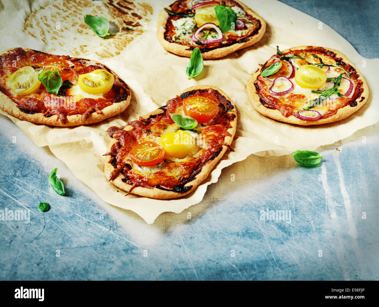 Quattro appena sfornato Italian mini pizza con un Formaggio, pomodoro e basilico fresco topping su grungy macchiato di carta forno con copyspace Foto Stock