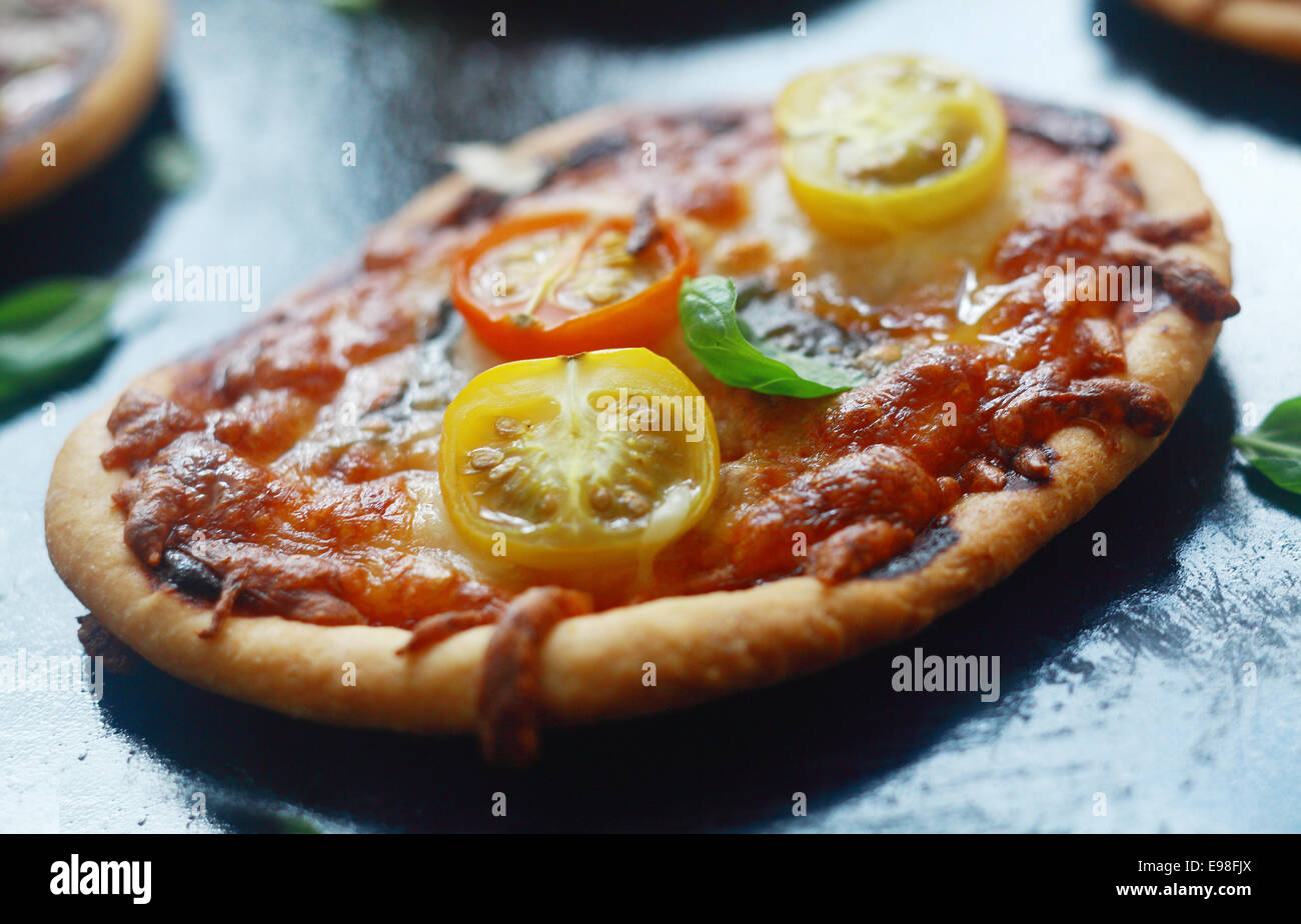 Italian mini pizza con formaggio e pomodoro su una spessa crosta dorata base condito con basilico fresco, vista ravvicinata Foto Stock