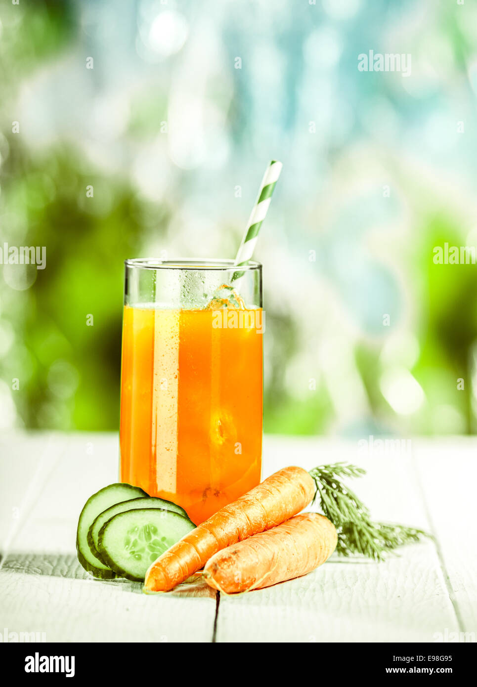 Vegetariano sano di carota e cetriolo cocktail realizzato dalla fattoria di ingredienti freschi e servito in un bicchiere con una cannuccia su un di legno bianco Tavolo picnic su un giorno di estate Foto Stock