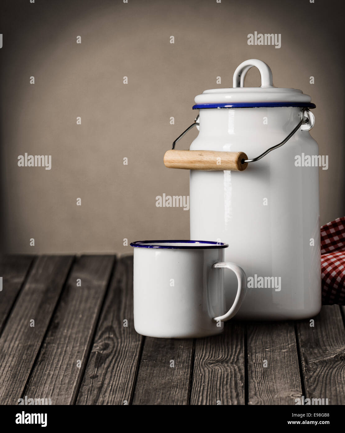 Bianco smaltato tin mug e cucina barattolo di storage con un coperchio e maniglia in piedi su un vecchio grunge contatore di legno con copyspace sulla parete dietro Foto Stock