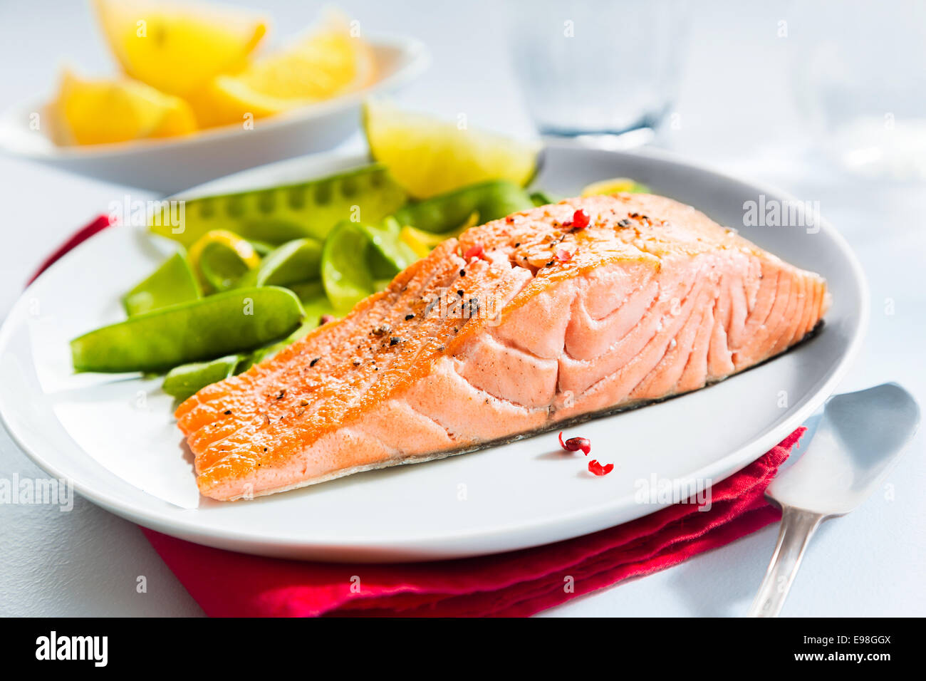 Gourmet pasto a base di pesce di salmone alla griglia bistecche servite con fresco verde taccole piselli e spicchi di limone per aromatizzare Foto Stock