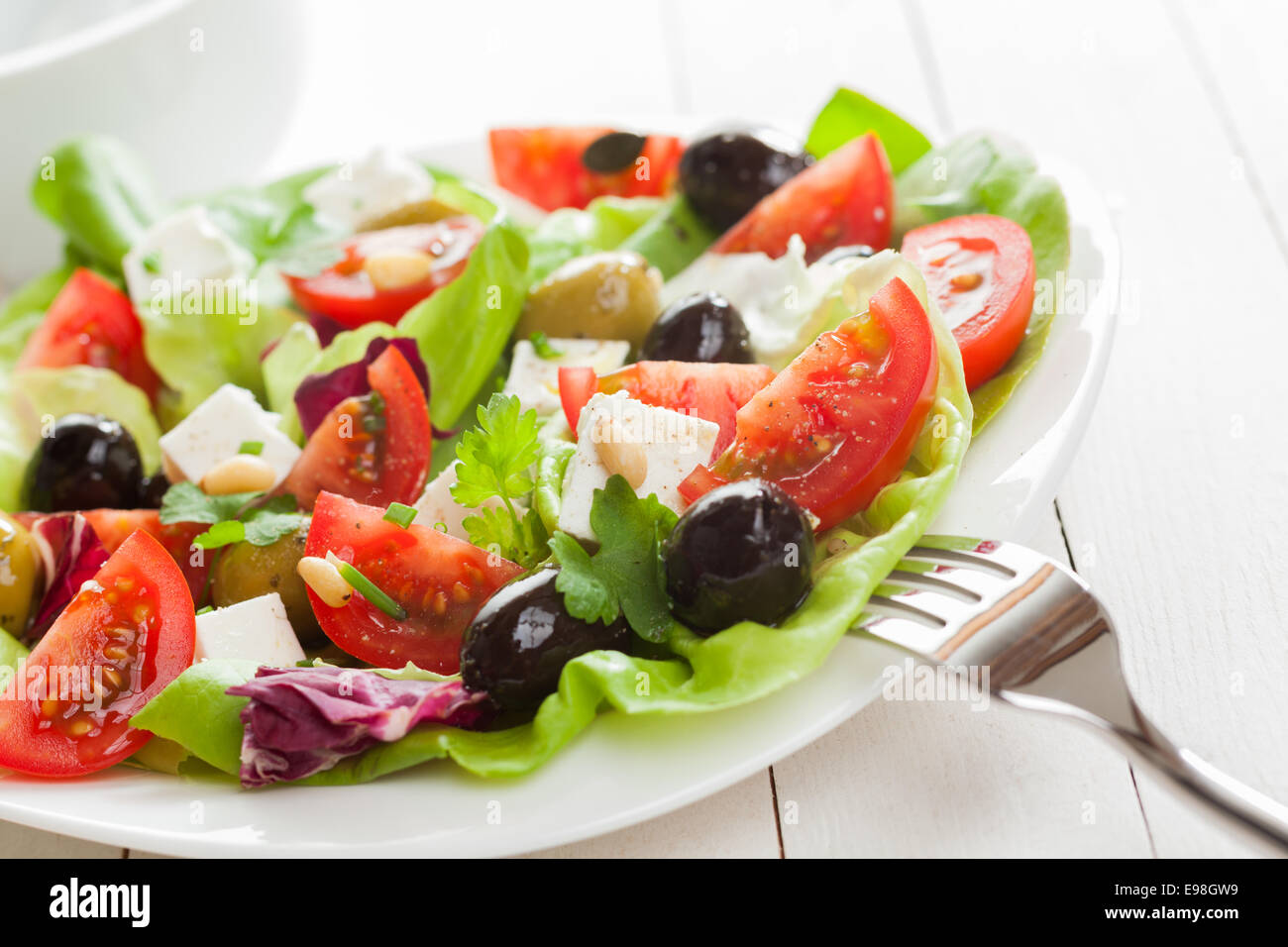 Una sana gustosa insalata mediterranea con pomodoro fresco, olive, il formaggio feta, di erbe e di lattuga, vista ravvicinata su una piastra Foto Stock