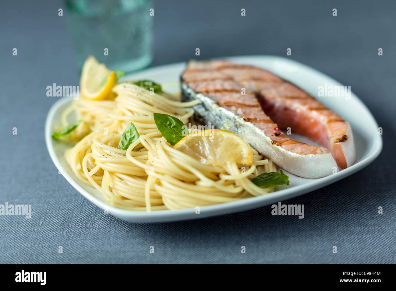 Italian linguine guarnita con foglie di basilico fresco servito con un gourmet alla brace bistecca di salmone per una deliziosa cena a base di pesce Foto Stock