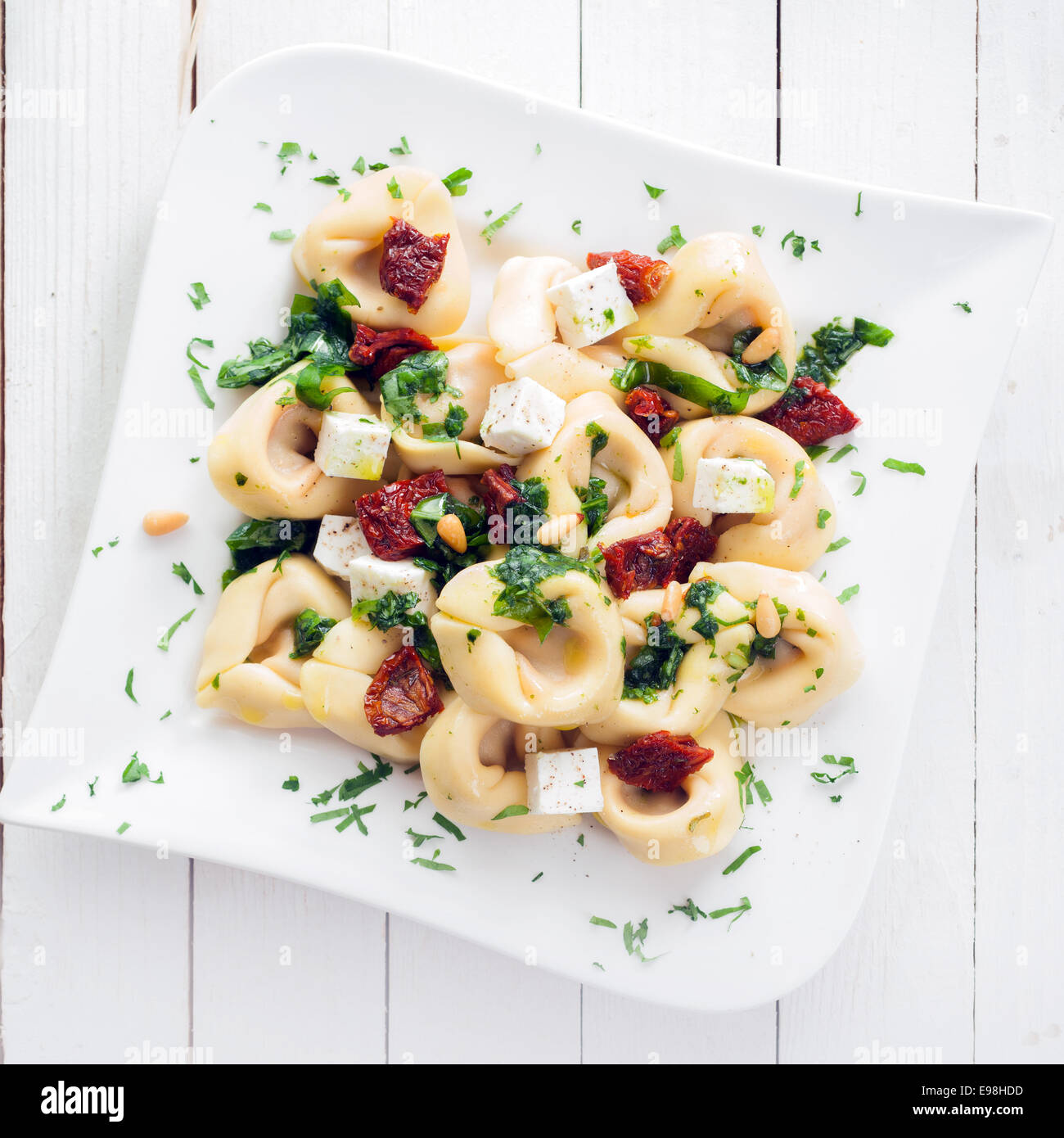 Vista in pianta di una piastra di insaccati tortellini italiana la pasta con il formaggio feta e pesto cosparso con erbe fresche e pinoli Foto Stock