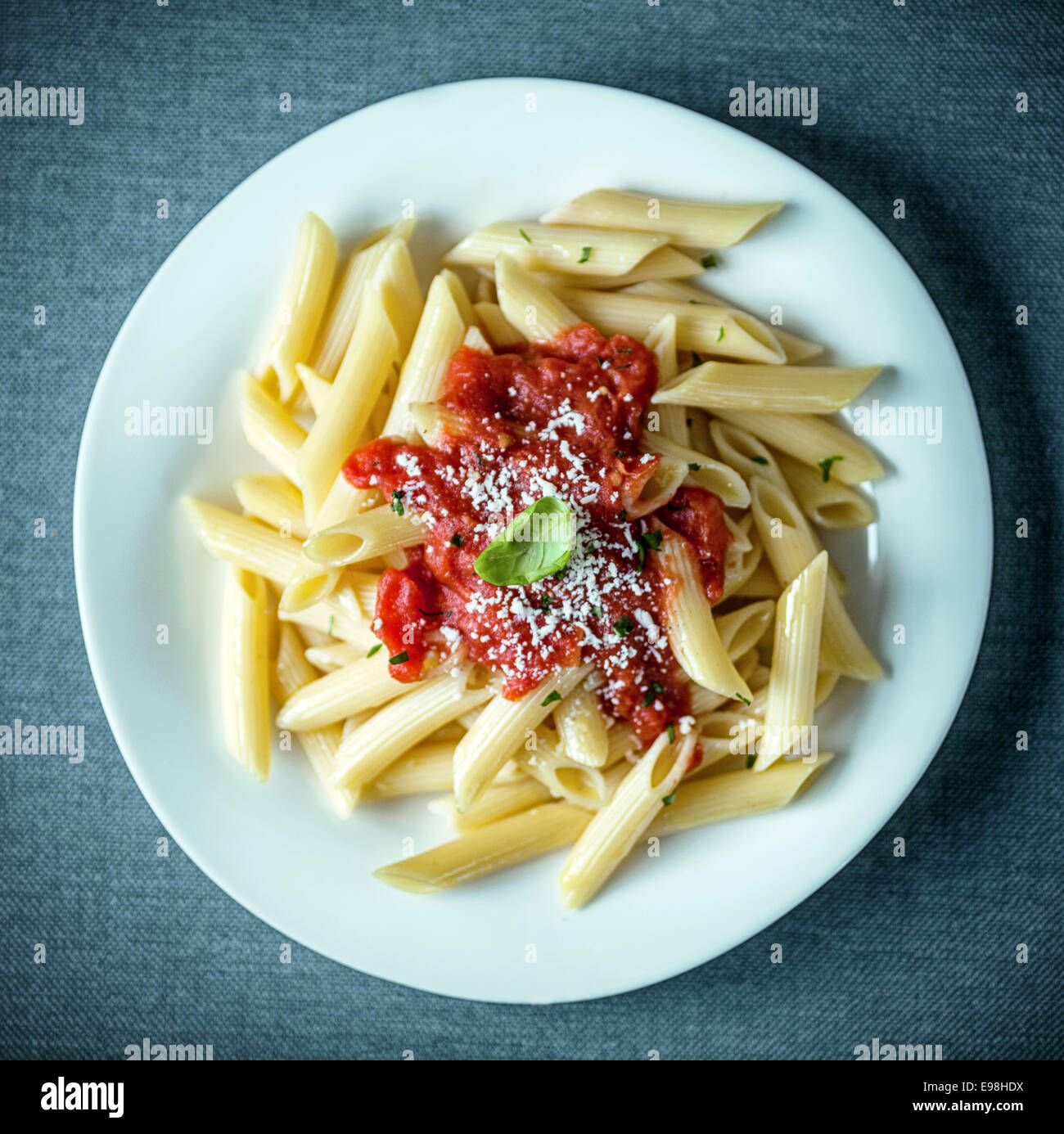 Italiano tradizionale di penne passati condito con una saporita piccante salsa di pomodoro cosparso con parmigiano grattugiato e guarnite con foglie di basilico fresco, vista aerea Foto Stock