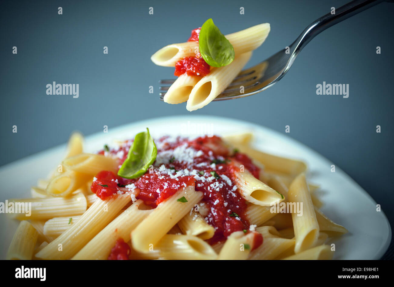 Mangiare un piatto di penne italiani pasta con tre noodles guarnita con un pizzichino di salsa di pomodoro e basilico fresco su una forcella al di sopra della piastra Foto Stock