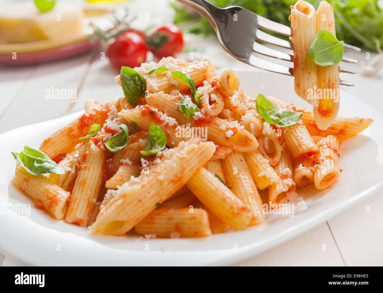 Deliziosi italiano penne rigate pasta con basilico fresco e parmigiano grattugiato servito con insalata con una forcella con due tubi di pasta sospesa al di sopra della piastra Foto Stock