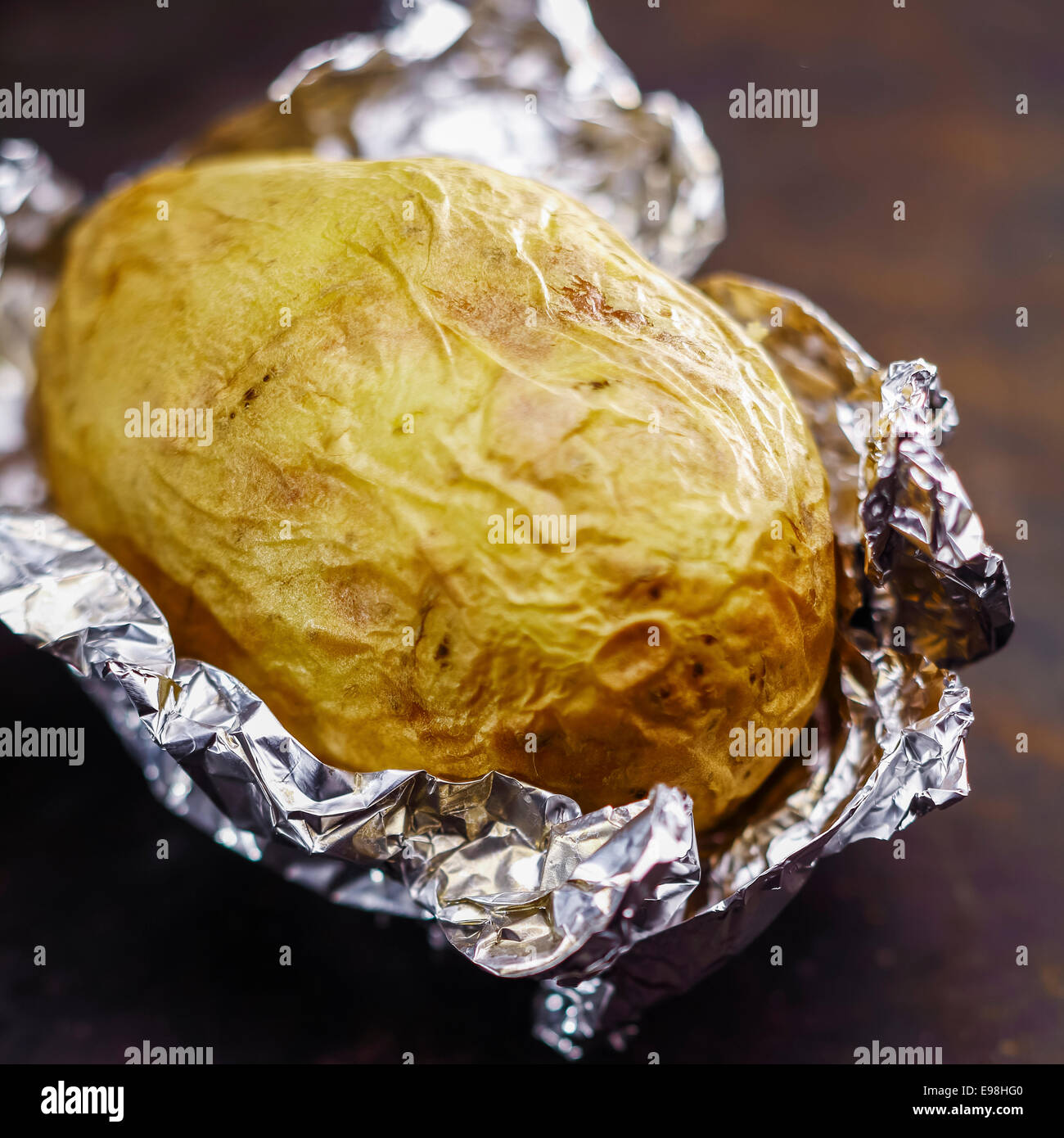 Delizioso caldo patate al forno in un foglio di alluminio fresco di estate barbecue che ancora giacciono sul suo avvolgimento in argento Foto Stock