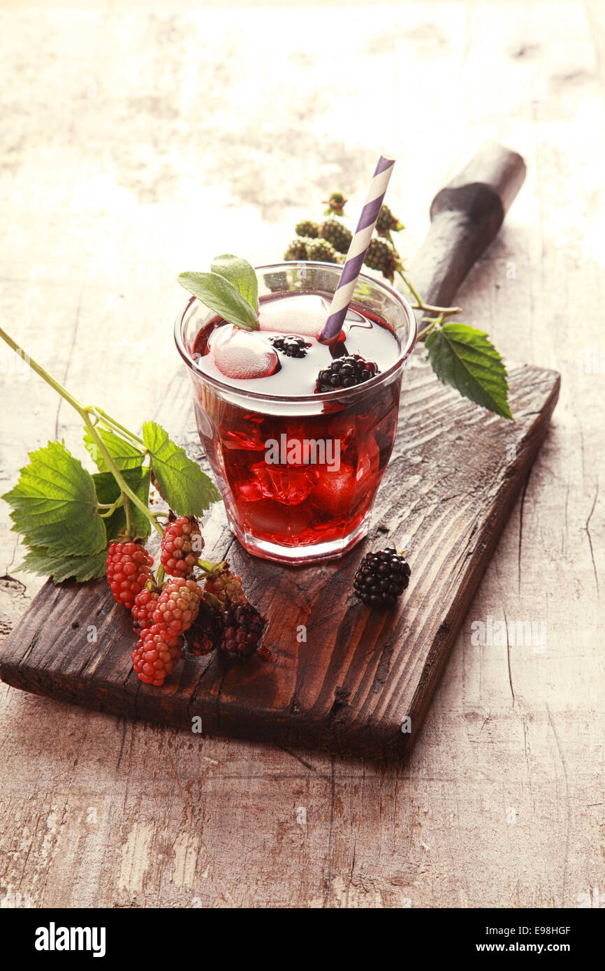 Bicchiere di succo di frutta su un rustico di legno aperto con more fresche e foglie di un sano ristoro estivo Foto Stock