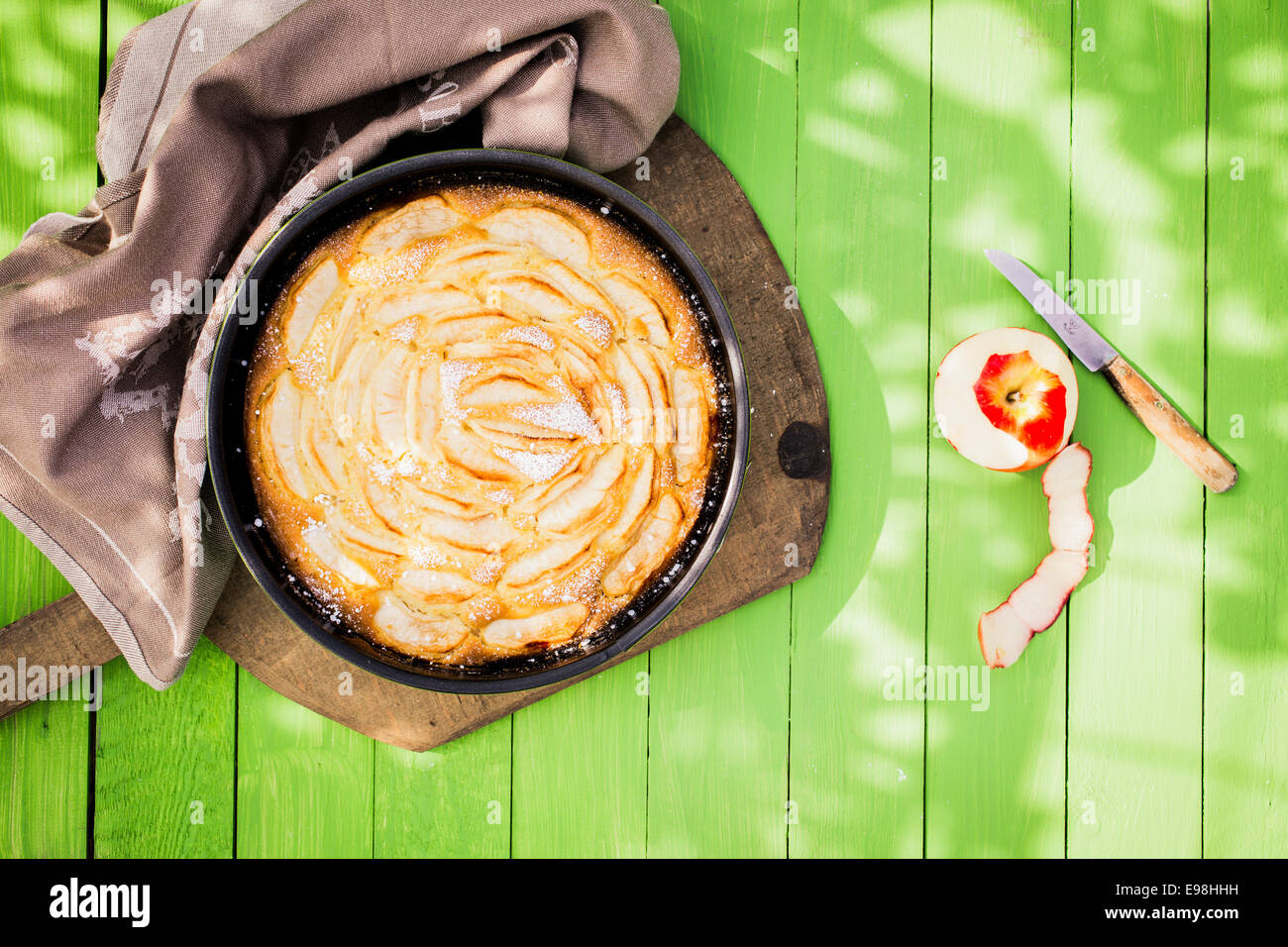 Una deliziosa casa dorata cotta la torta di mele è vista dal di sopra in una teglia da forno su un verde giardino in legno tavolo in pezzata luce solare per un rilassante pasto estivo e dessert Foto Stock