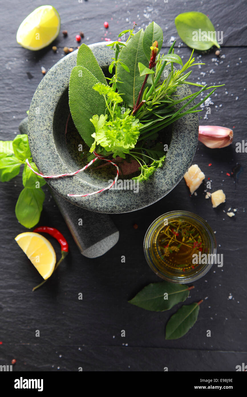 Un assortimento di aromatiche fresche erbe culinarie in un pestello e mortaio con aglio e condito da olio di oliva sul lato, vista aerea su ardesia con copyspace Foto Stock