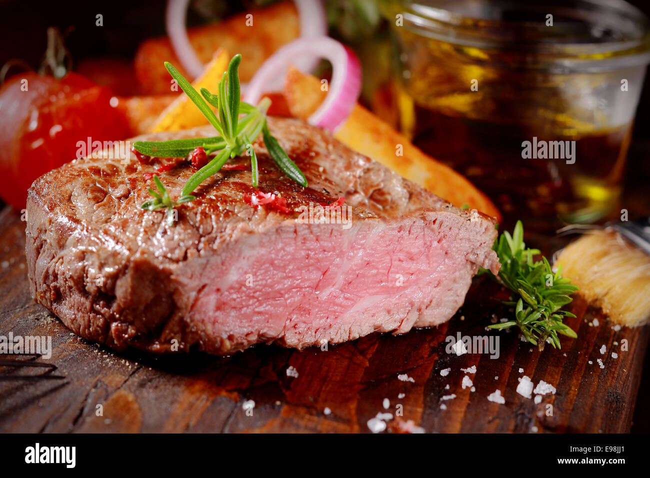 Succulente rare tenera bistecca grigliata alla perfezione attraverso a fette per mostrare la texture condito con rosmarino fresco e sale Foto Stock