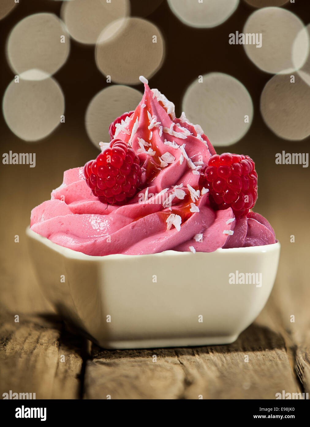 Gustosa berry yogurt congelato una spruzzata di sciroppo e decorate con lamponi freschi per un colorato dessert partito contro un bokeh di fondo Foto Stock