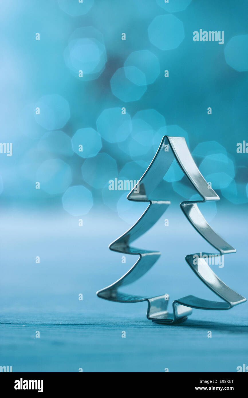 Albero di natale cookie cutter decorazione su un freddo inverno sfondo blu con una finta bokeh di partito e luci copyspace per i vostri auguri di Natale Foto Stock