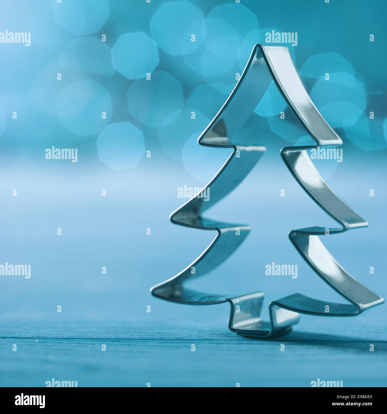 Argento lucido formina albero di natale decorazione su un freddo invernale sfondo blu con un bokeh di scintillanti luci di partito e copyspace , formato quadrato Foto Stock