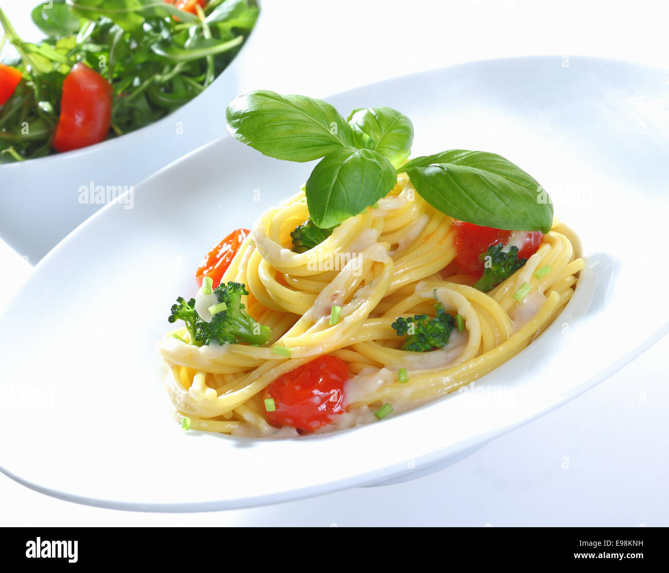 Spaghetti con broccoli e pomodoro con una crema di formaggio e salsa di basilico. Rucola pomodoro e insalata di mais in background. Foto Stock