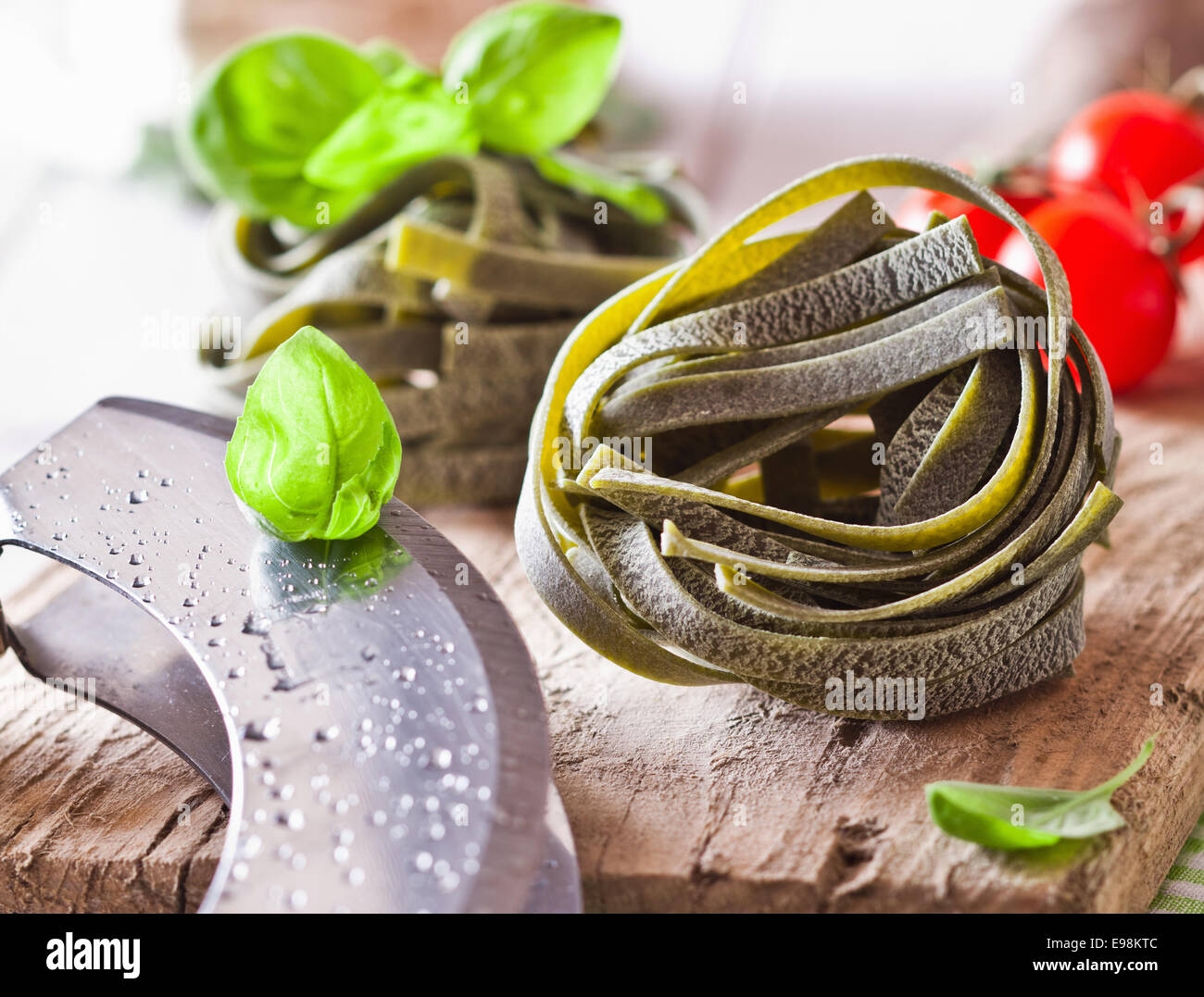 Nastro crudo Tagliatelle avvolto in una sfera in piedi su un rustico di una superficie di legno con basilico fresco e pomodori per la realizzazione di un piatto di pasta. Foto Stock