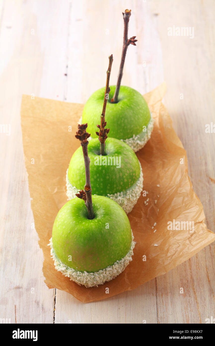 Fila di fresche mele verdi con ramoscelli per steli immerso in bianco zuccherini e servita come favori di Halloween per bambini trucco-o-trattare su carta marrone Foto Stock