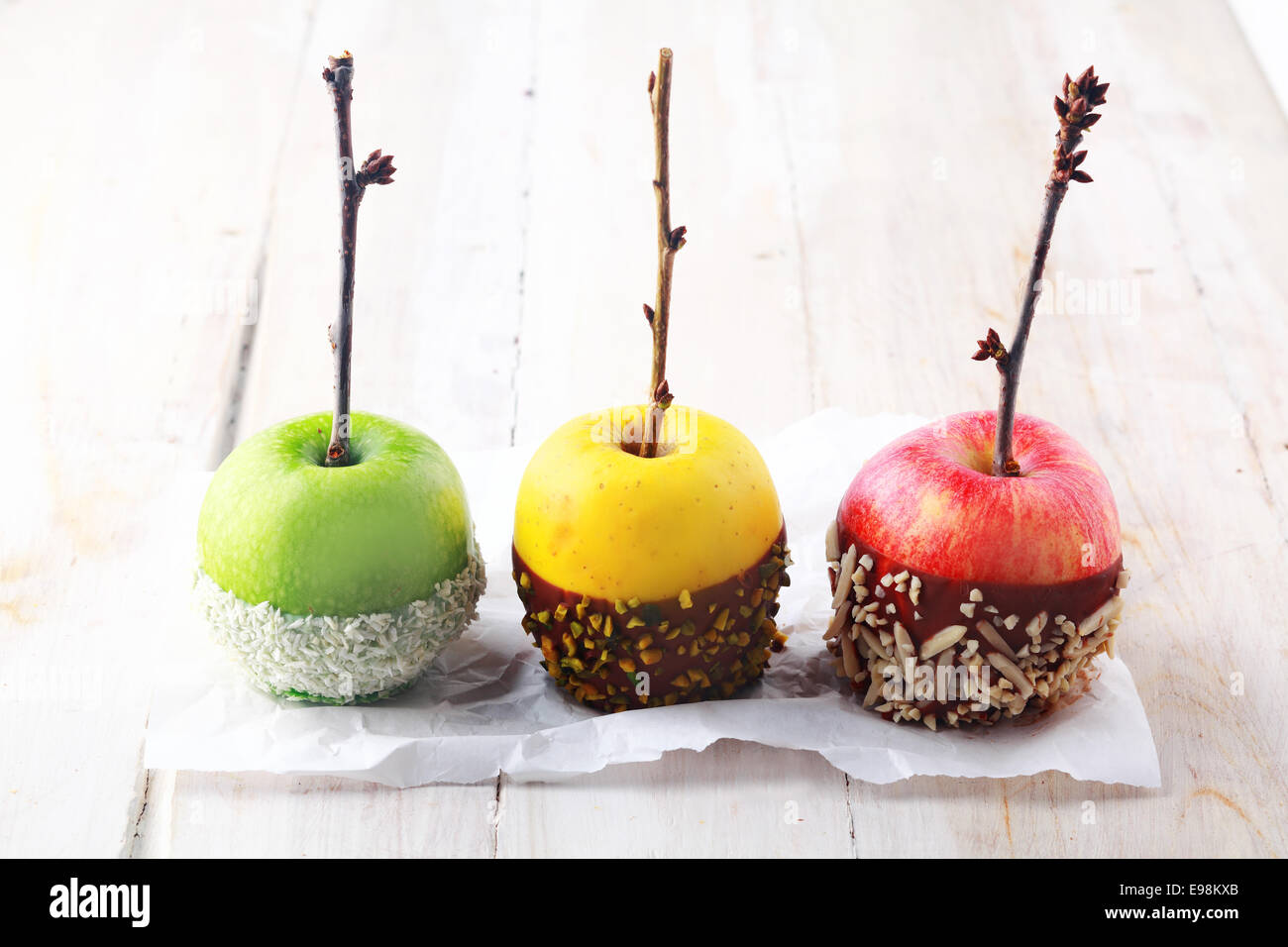 Tre colorate di rosso, verde e giallo Halloween fresche Mele immersi nel cioccolato e decorate con dadi e irrora con ramoscello Foto Stock