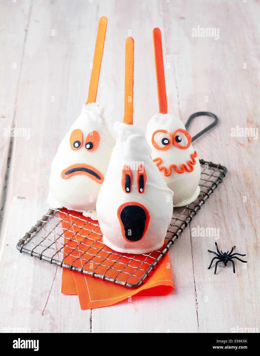 I fantasmi di trucco commestibili-o-trattare Halloween tratta fatto da pere fresche rivestito in marzapane e cioccolato con divertenti espressioni spaventoso con orange highlights raffreddare su una griglia a fianco di un ragno Foto Stock