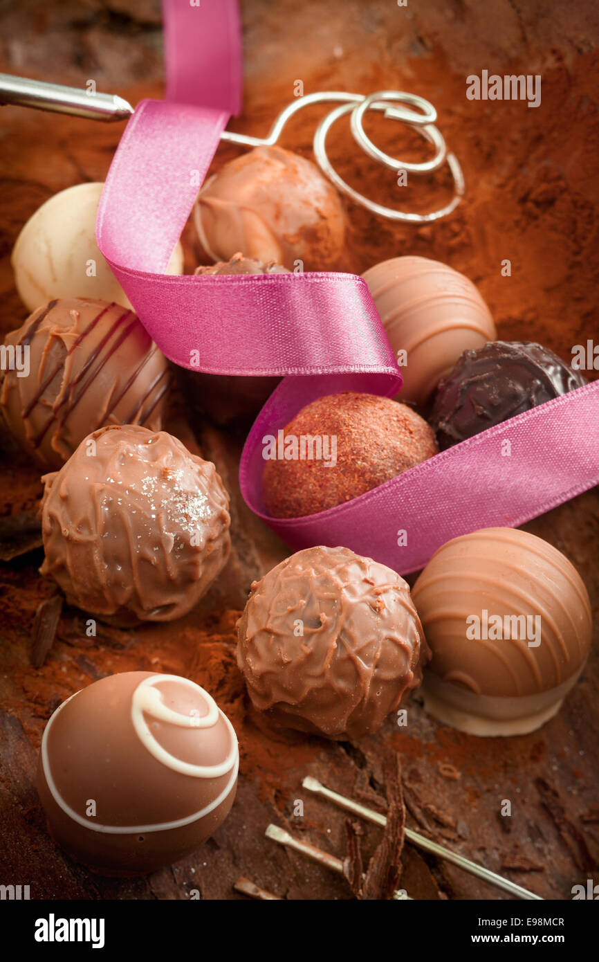 Lusso decorativo cioccolatini fatti a mano su un letto di polvere di cacao con un spiralata nastro rosa per una celebrazione o dono Foto Stock