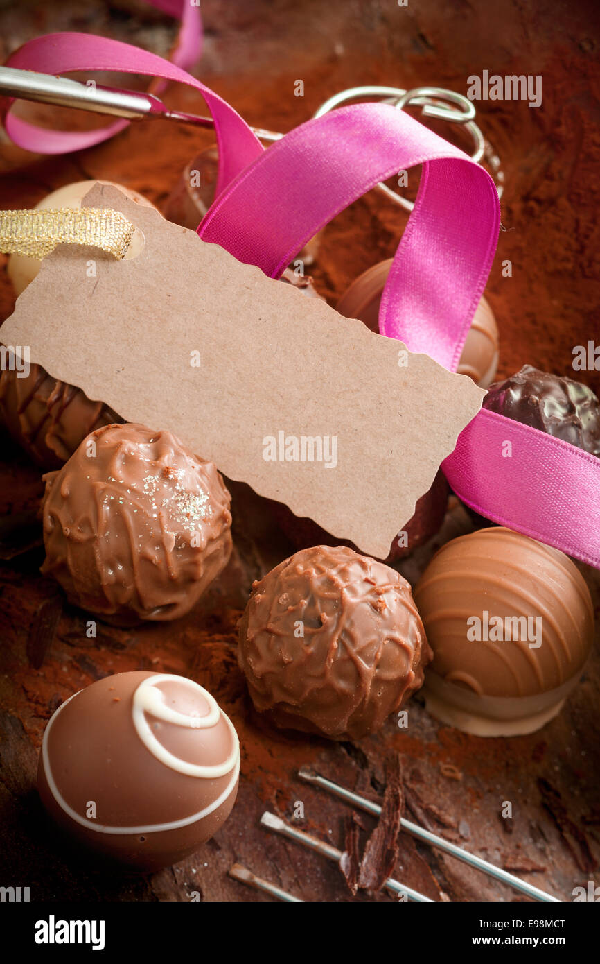 Fatte a mano deliziosi cioccolatini decorativa con un nastro rosa e un lusso testured blank gift tag con un bordo dentellato Foto Stock
