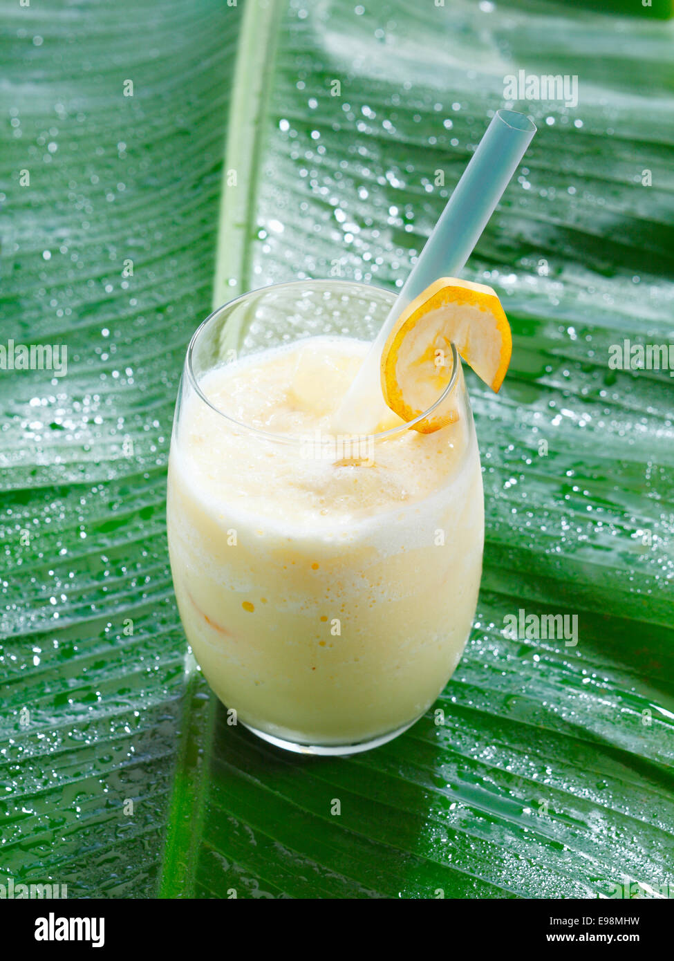 Angolo di alta vista di un singolo bicchiere di fresco frullato di banana o miscelato cocktail serviti su una banana frond con copyspace Foto Stock
