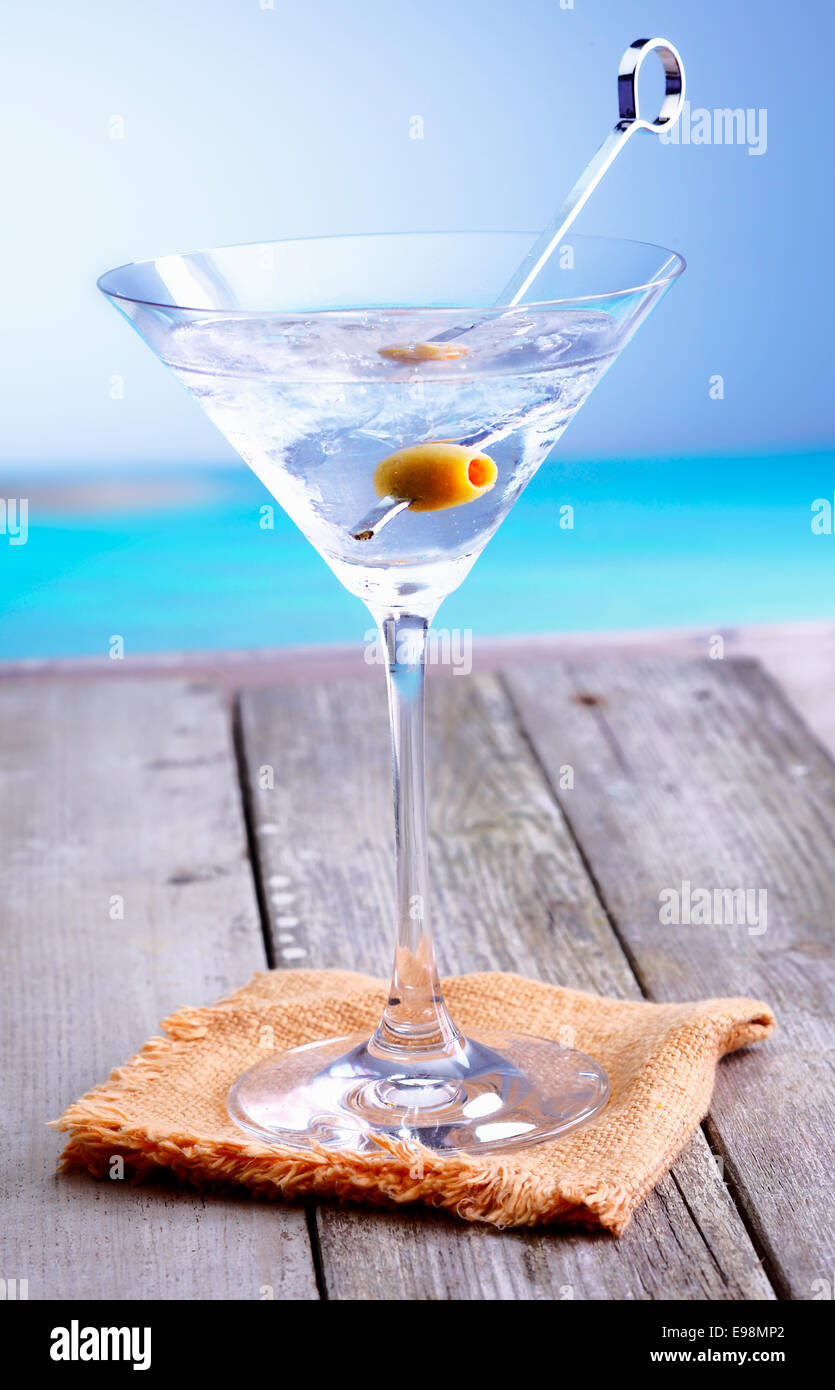 Rinfrescanti cocktail Martini in un bicchiere conico con olio di oliva guarnite servita su un deck di estate che si affacciano sull'oceano Foto Stock