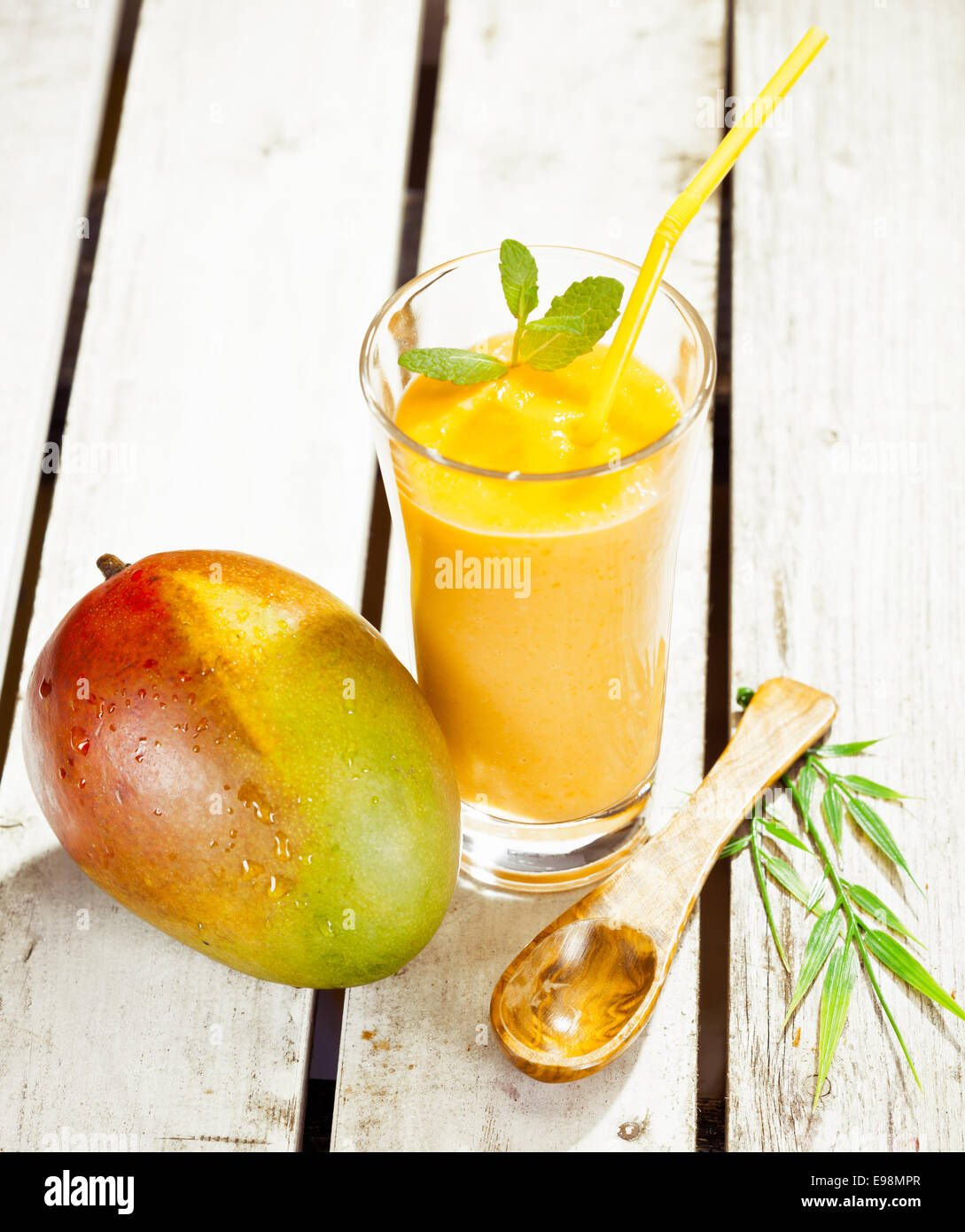 Elevato angolo di visione di un vetro sano di mango fresco smoothie con una deliziosa mature frutta intera a fianco sul decking in legno Foto Stock