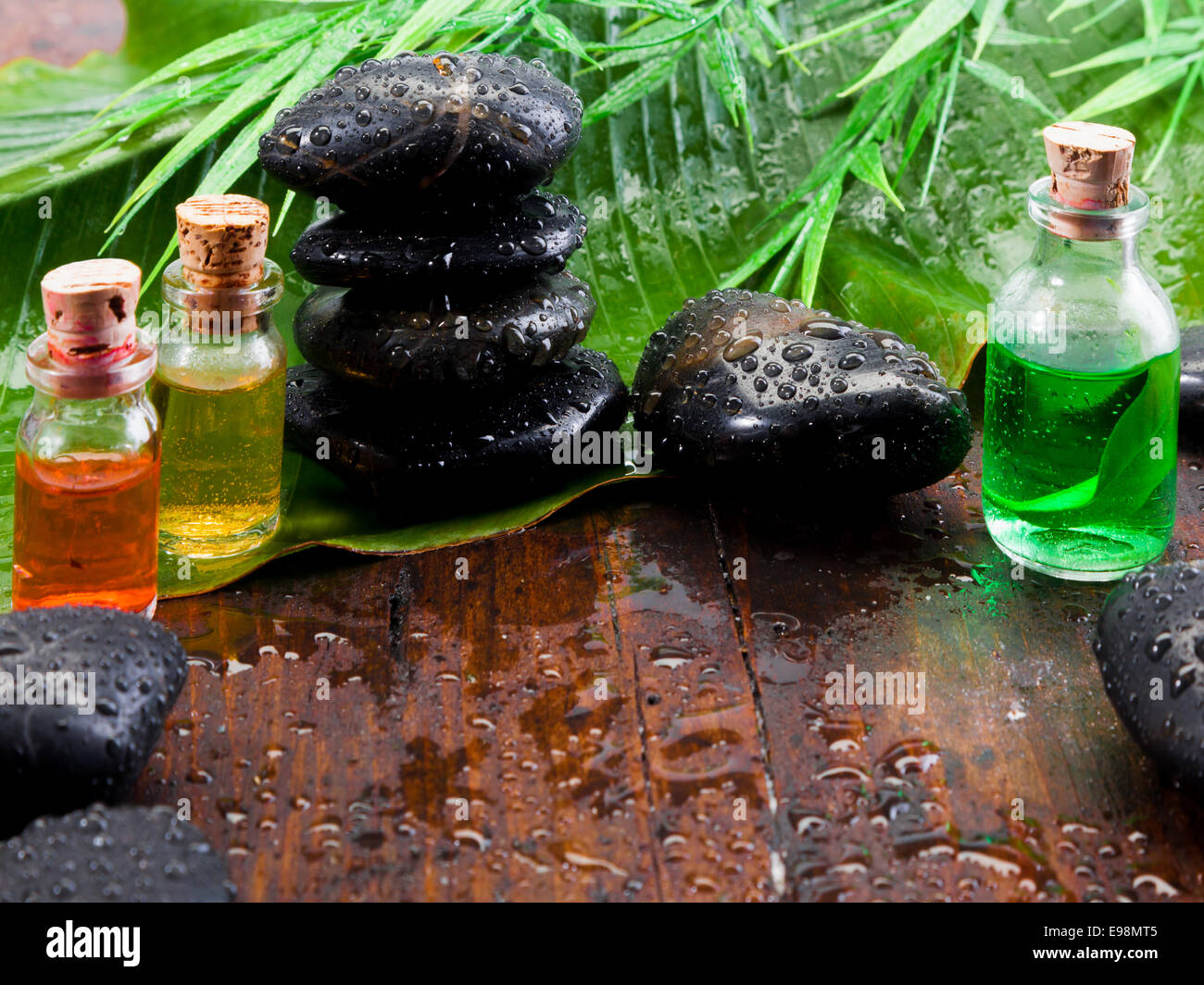 Bottiglie di olio essenziale di estratti vegetali e smooth black pietre massaggio in aromaterapia un trattamento spa still life Foto Stock