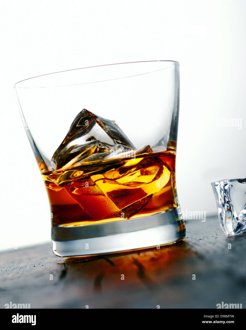 Immagine angolata di un bicchiere di whiskey d'oro o di brandy su rocce con grandi cubetti di ghiaccio è servito su un bancone bar Foto Stock