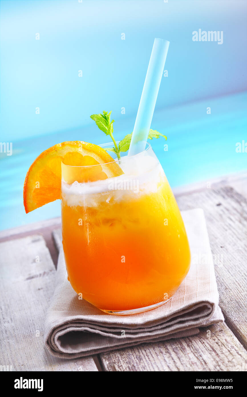 Iced rinfrescanti cocktail arancione in piedi su un ponte di legno che si affacciano sull'oceano in vacanza in un resort tropicale Foto Stock
