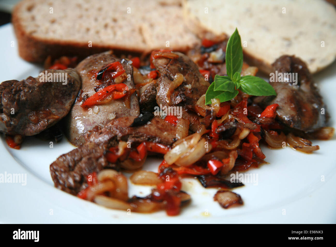 Pan fried fegatini di pollo con cipolle caramellate e peperoni rossi serviti sulla piastra bianca con marrone e il pane di segale e basilico Foto Stock