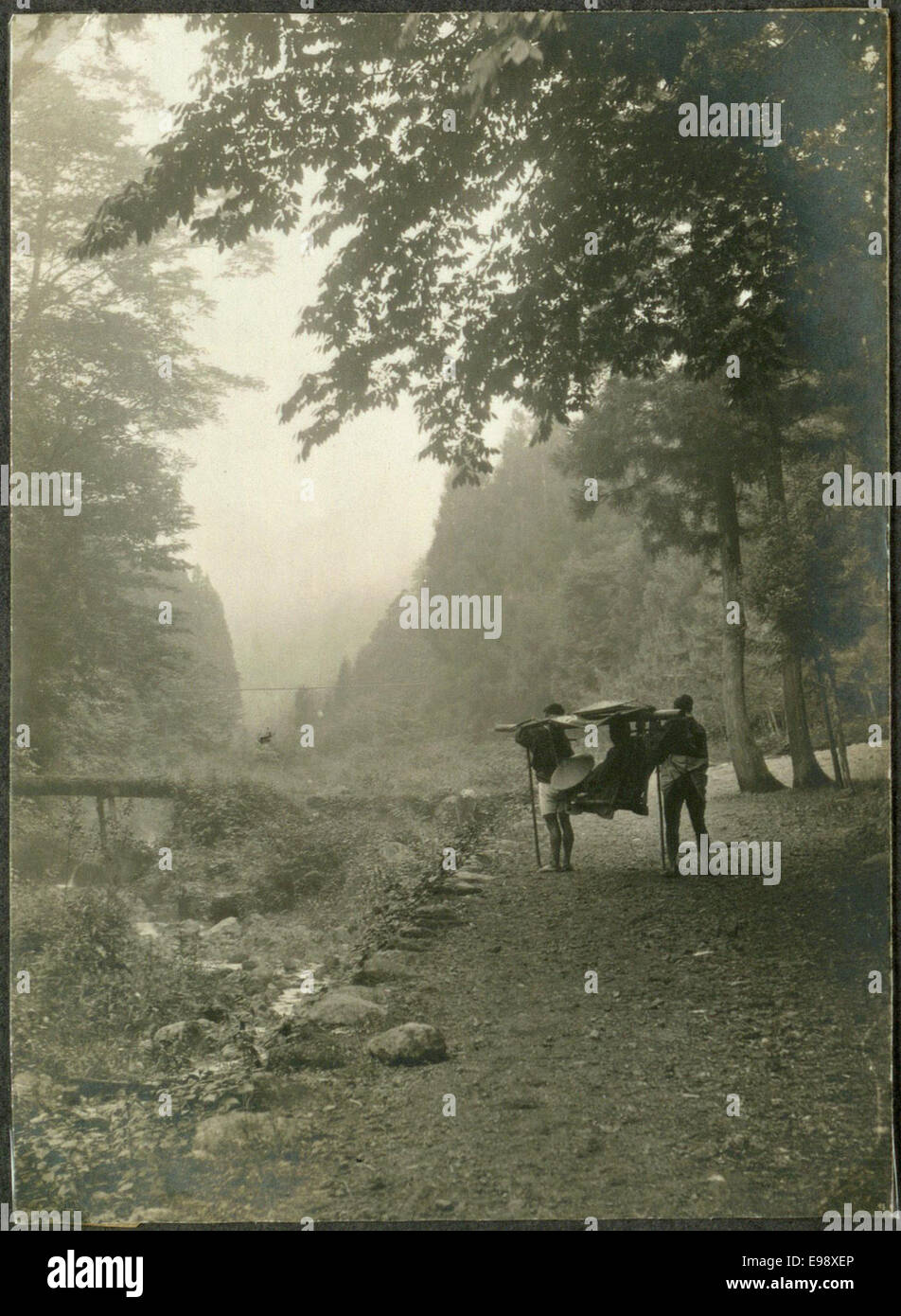 Una fotografia storica di un viaggiatore trasportato su una sedia berlina (lettiera) in Giappone, che mostra i metodi di trasporto tradizionali utilizzati nella regione durante l'inizio del XX secolo. Foto Stock