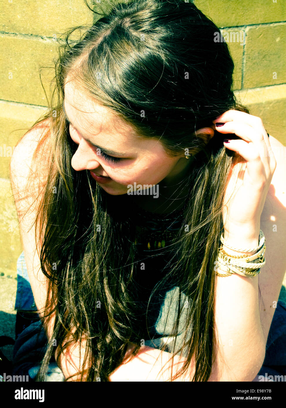 Giovane ragazza seduta in sun capelli soffiando nel vento Foto Stock