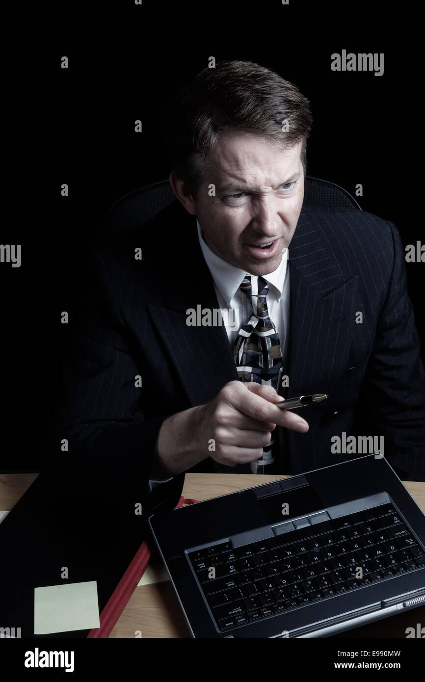L'immagine verticale dell uomo d affari, esprimendo rabbia guardando sullo schermo del computer, lavora fino a tardi con sfondo nero Foto Stock