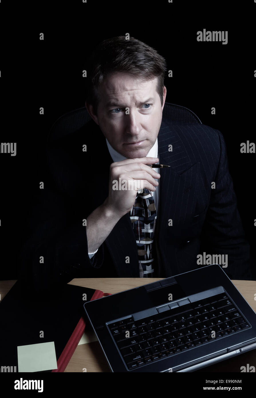 L'immagine verticale dell uomo d affari e guardando lo schermo del computer mentre si tiene la penna, lavora fino a tardi con sfondo nero Foto Stock