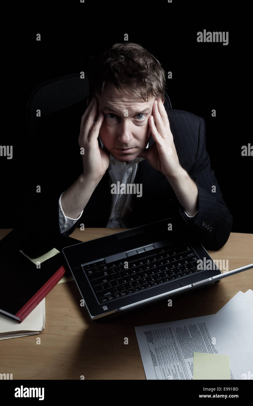 L'immagine verticale di uno stanco uomo d affari lavorare fino a tarda notte con sfondo nero Foto Stock