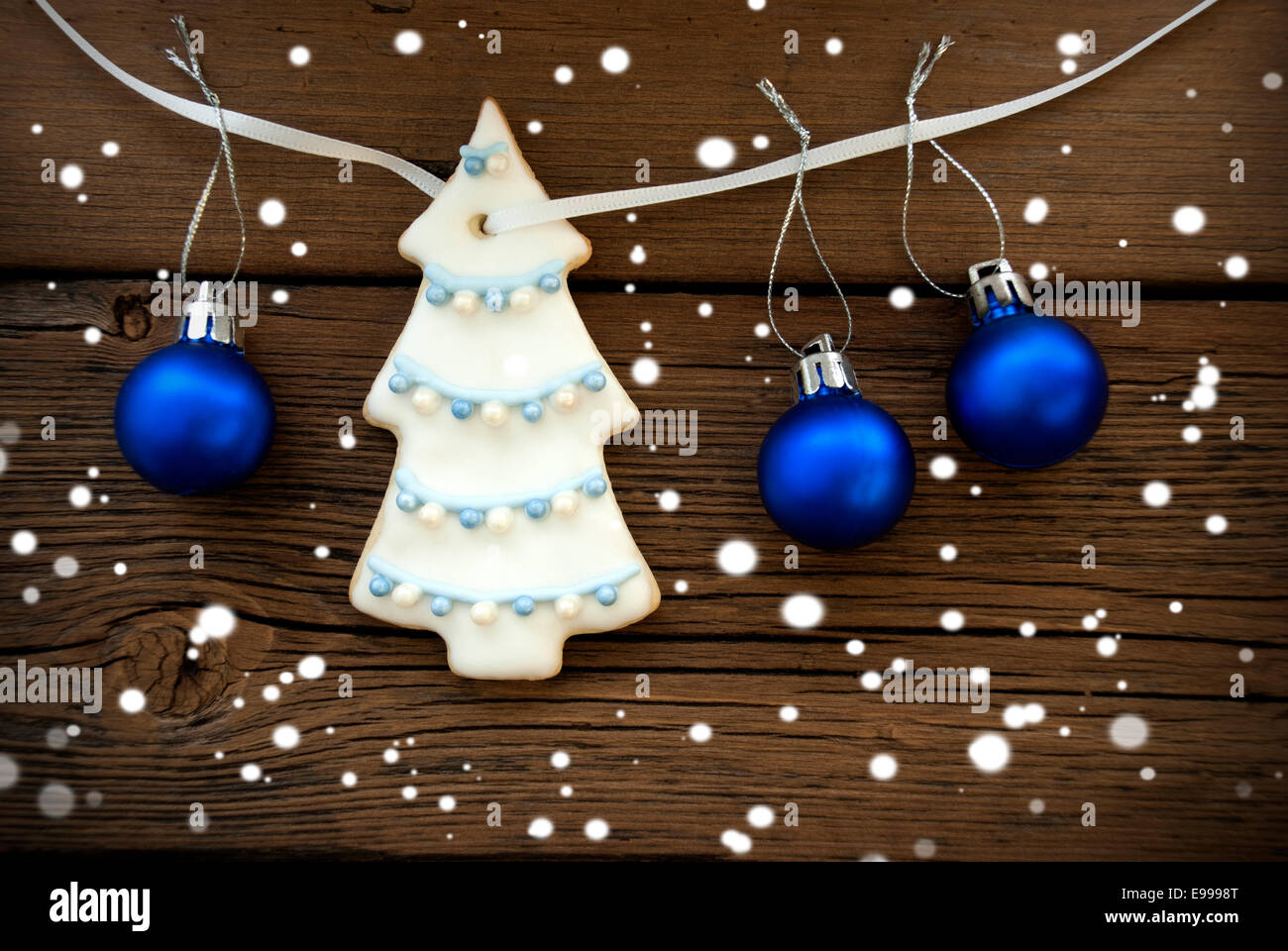 Albero di Natale Cookie con decorazione e tre palle di Natale appeso su una linea su legno Bckground con i fiocchi di neve Foto Stock