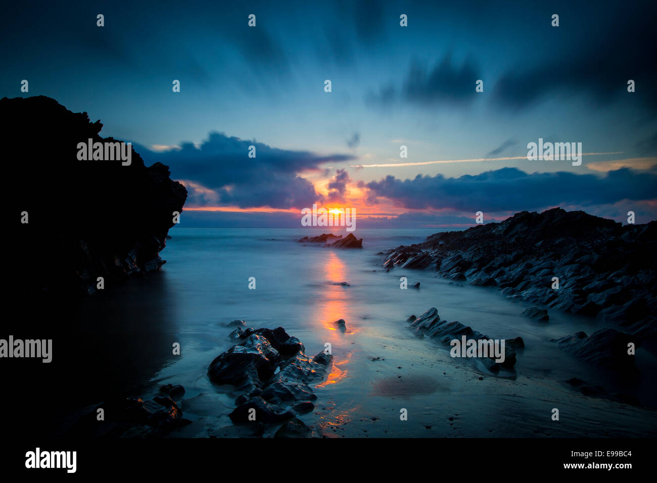 Nuvoloso Tramonto su scogli lungo la costa della Cornovaglia vicino a Newquay, Cornwall, Inghilterra Foto Stock
